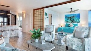 A modern living room with a sofa, two armchairs, a coffee table, and a dining area with a kitchen in the background. - Alii Villas #332 Million Dollar Ocean View. Watch Dolphins, Coastal Vibes. (Kailua-Kona)