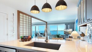 A modern kitchen with a large island, pendant lights, and a view of the sea through large windows. - Alii Villas #332 Million Dollar Ocean View. Watch Dolphins, Coastal Vibes. (Kailua-Kona)