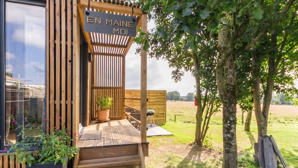 A wooden deck with a pergola, a potted plant, and a sign reading "EN MAINE MOI...".