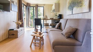 A modern living room with a sofa, a wooden stool, and a coffee table. There is a TV mounted on the wall and a painting above the sofa.