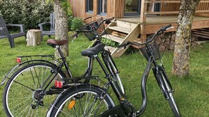 Two bicycles parked on a grassy area with a wooden deck and a modern building in the background.
