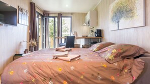 A bedroom with a large bed, a desk, a chair, and a TV on the wall.