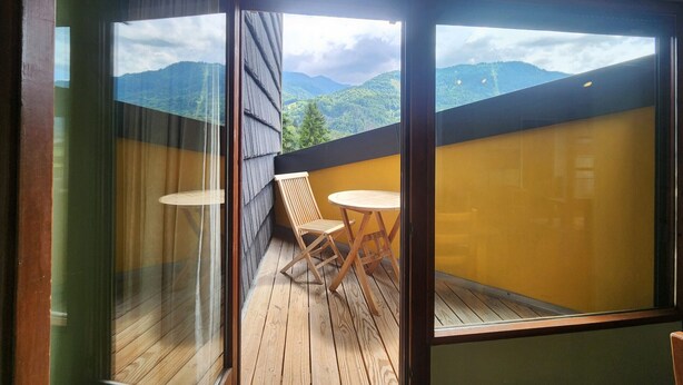 Ein Balkon mit Holzboden, zwei Holzstühlen und einem Tisch.