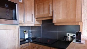 A kitchen with wooden cabinets, a Bosch microwave, a black countertop, a sink, and a kettle. - Pleasant mountain-style apartment for 6 near shops and cable cars (Le Grand-Bornand)