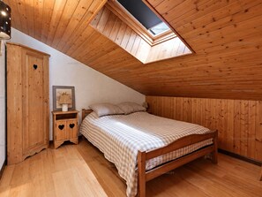 A bedroom with a sloped ceiling, wooden walls, a bed with a checkered bedspread, a bedside table with a lamp, and a framed picture on the wall. - Pleasant mountain-style apartment for 6 near shops and cable cars (Le Grand-Bornand)