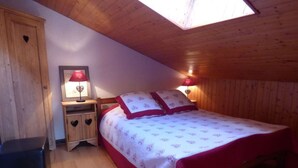 A bedroom with a wooden ceiling, a bed with red and white bedding, two bedside lamps, and a small wooden cabinet with heart-shaped cutouts. - Pleasant mountain-style apartment for 6 near shops and cable cars (Le Grand-Bornand)
