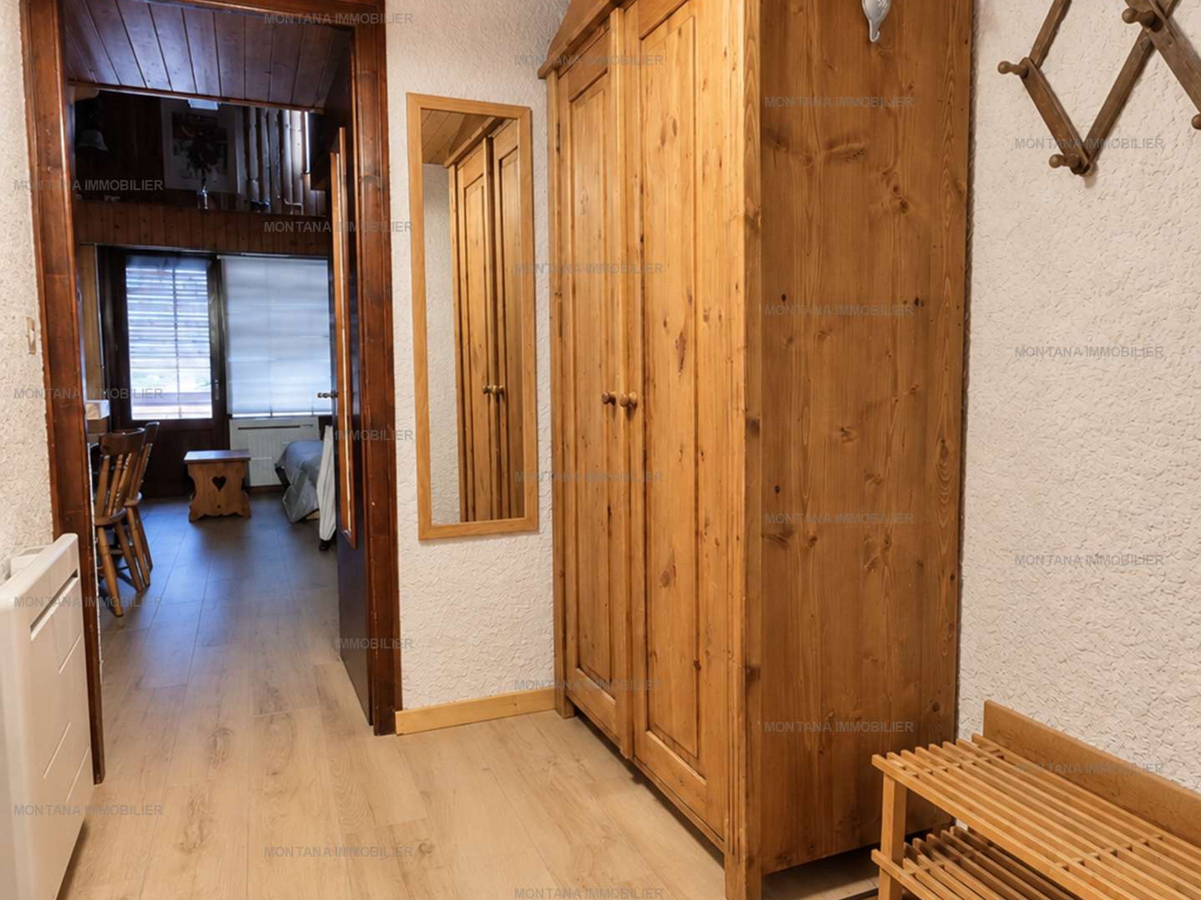 A wooden interior with a wardrobe, a bench, and a dining area with chairs and a table.