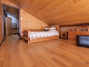 A bedroom with a wooden ceiling, a bed with a checkered bedspread, a nightstand, a dresser, and a small table with decorative items. - Pleasant mountain-style apartment for 6 near shops and cable cars (Le Grand-Bornand)