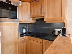 A kitchen with wooden cabinets, a Bosch microwave, a kettle, and a coffee maker on the counter. - Pleasant mountain-style apartment for 6 near shops and cable cars (Le Grand-Bornand)