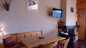 A cozy room with a wooden table, a bench, a television mounted on the wall, and a fireplace. - Pleasant mountain-style apartment for 6 near shops and cable cars (Le Grand-Bornand)