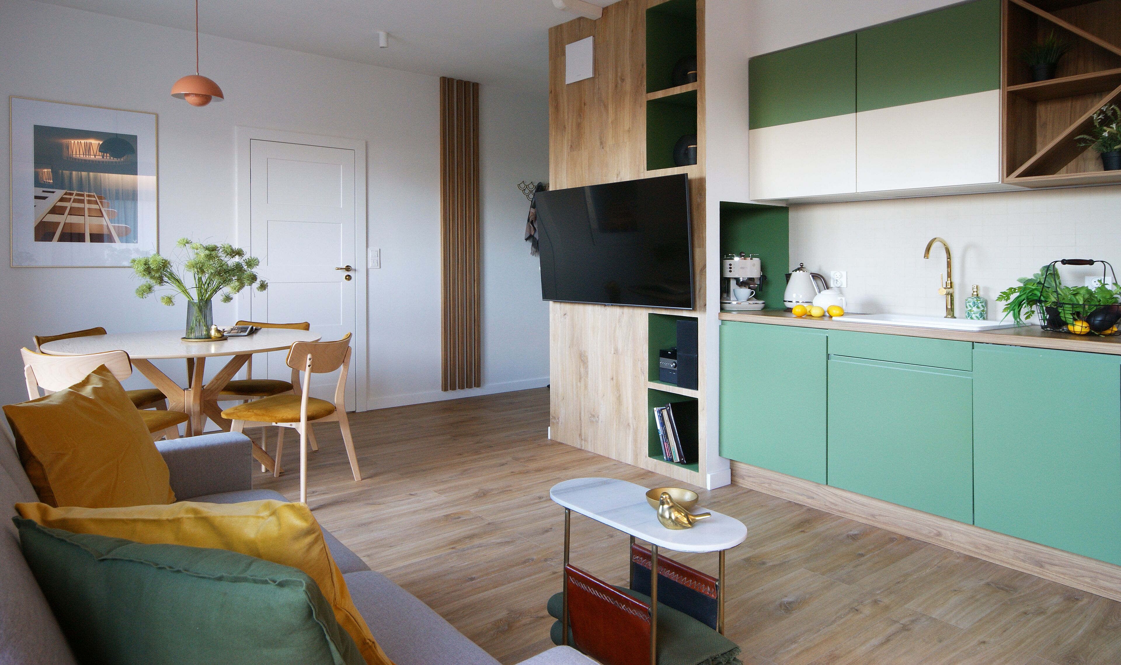 Una sala de estar moderna con sofá, mesa de comedor y zona de cocina con armarios verdes y televisor.