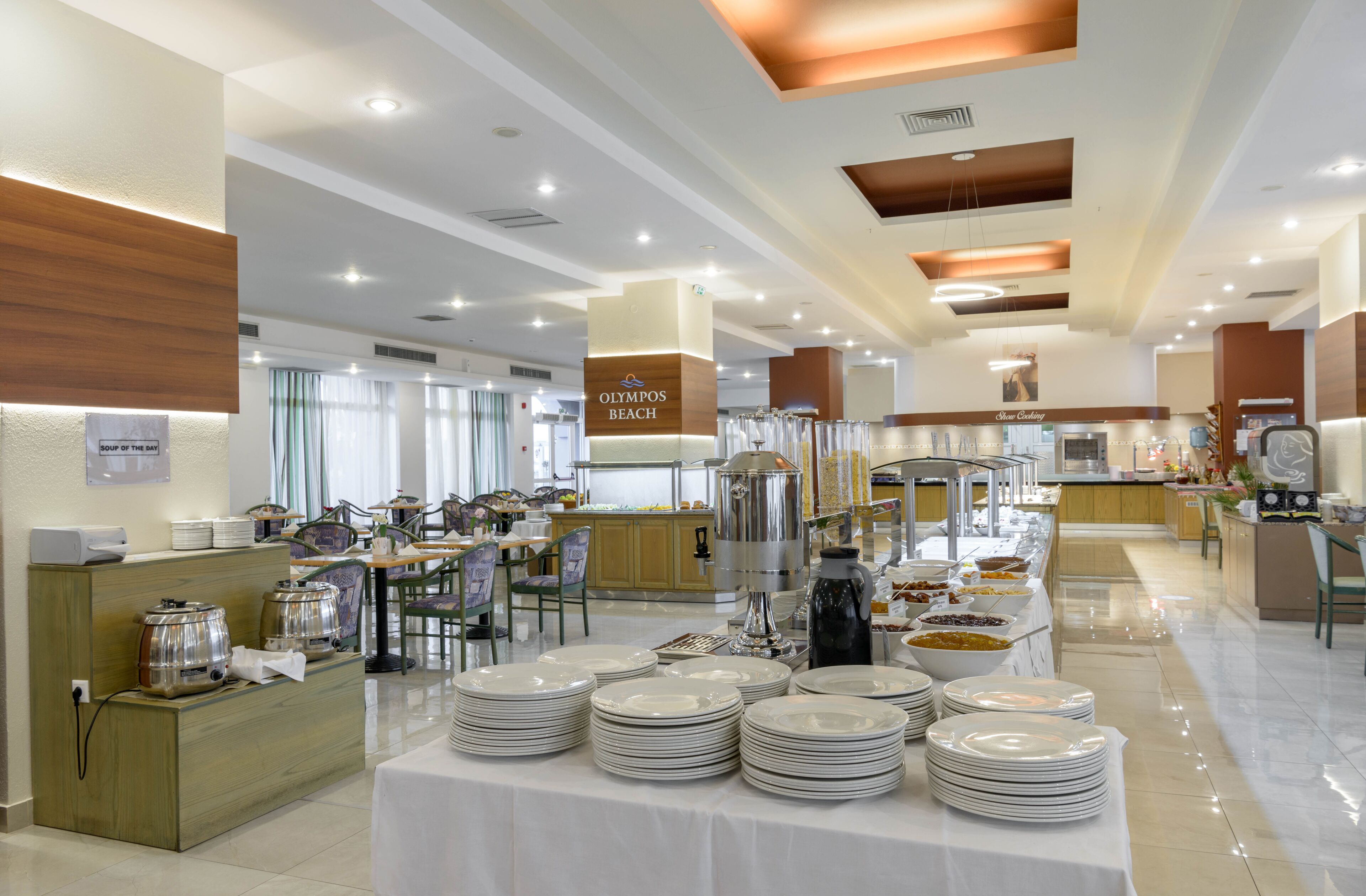 Un buffet est installé dans un hôtel, avec plusieurs points de service, une table de buffet centrale où les assiettes sont empilées, et une cuisine en arrière-plan.