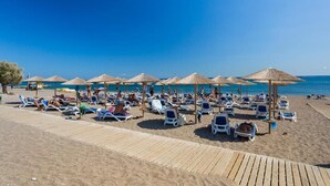 A beach with sun loungers and umbrellas, a wooden boardwalk, and the sea in the background. - Olympos Beach (Rhodes)