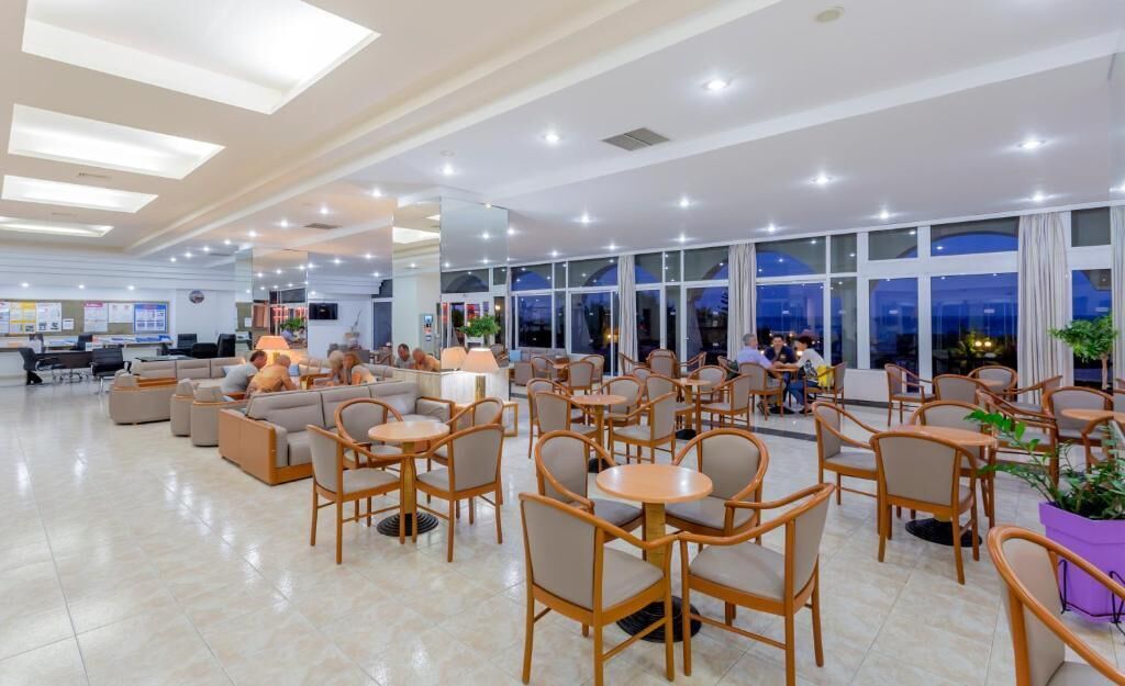 Un amplio vestíbulo de hotel con varias zonas de estar, incluidas sofás y mesas, y un gran ventanal que ofrece vistas del cielo nocturno.