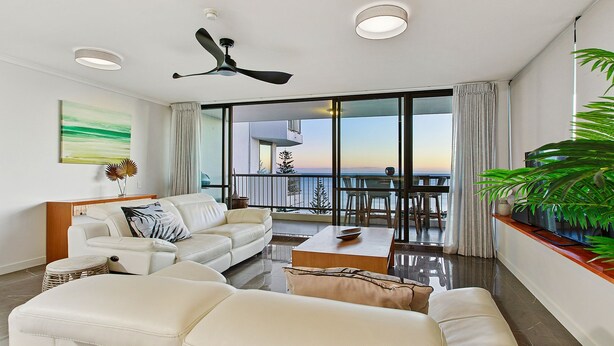 Un salón amplio con sofá blanco, una mesa de centro y un balcón con vistas al mar.