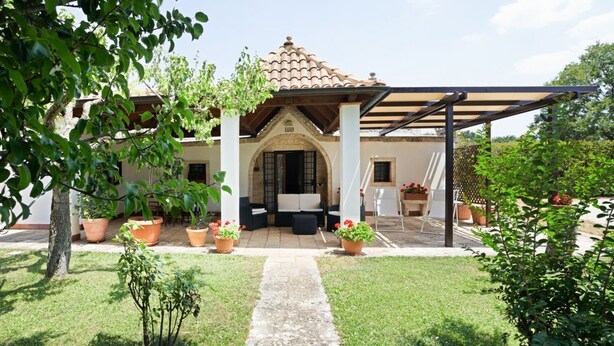 Une maison dotée d’un patio couvert, d’un chemin en pierre et de plantes en pot.