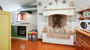 Une cuisine avec une cheminée en pierre, des murs carrelés, un fourneau et un four à micro-ondes.