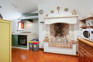 A kitchen with a stone fireplace, tiled walls, a stove, and a microwave.