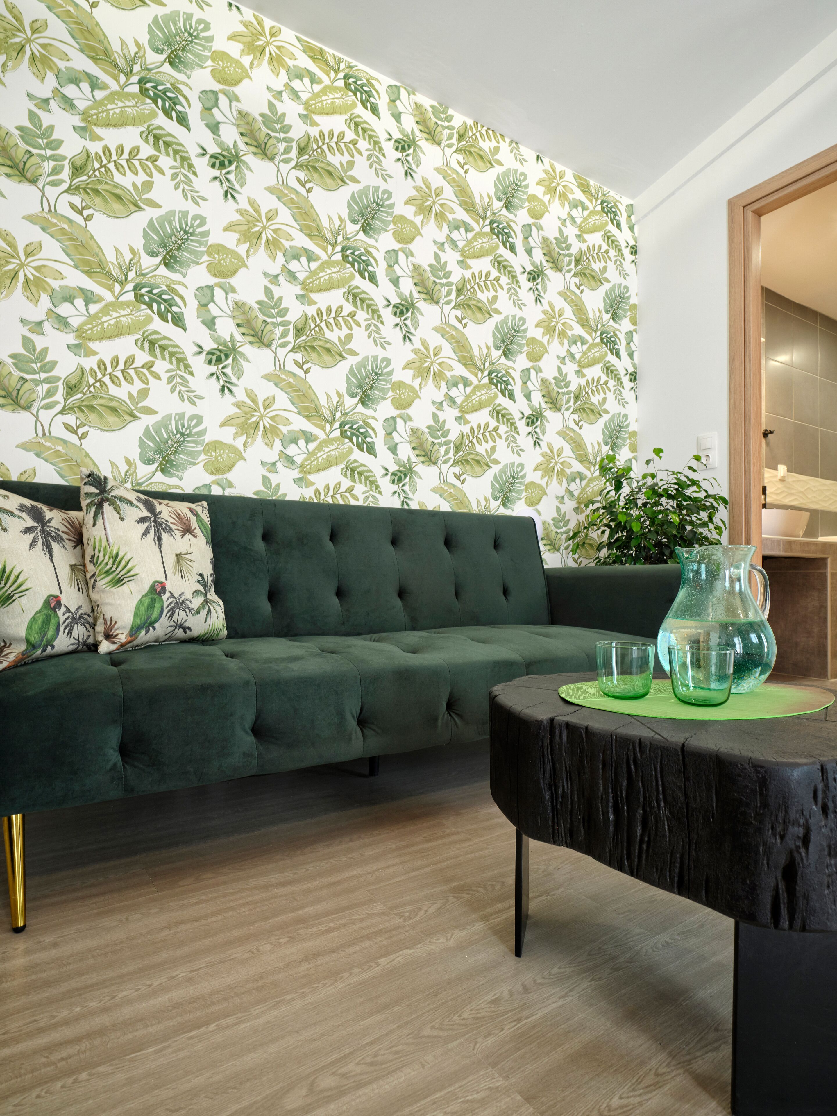 A living room with a green sofa, a patterned wallpaper, a wooden coffee table, and a potted plant.