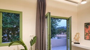 Una habitación con techo de madera, puerta corredera de vidrio, planta en maceta, una mesita y un estante en la pared con una escultura.