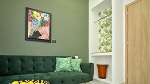 Un sofá verde con cojines estampados, suelo de madera, un cuadro colgado en la pared y una cesta de limones.