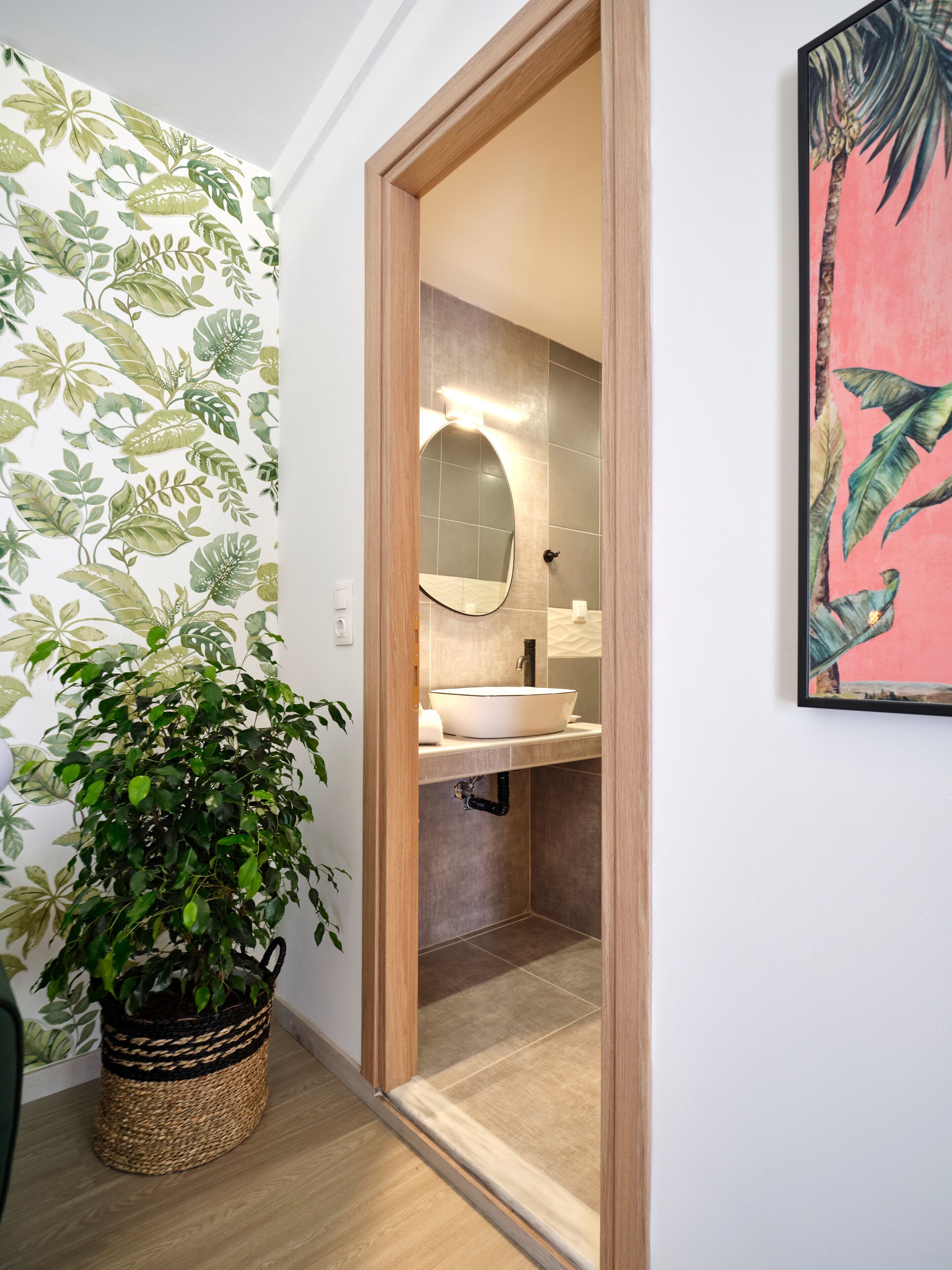 Une salle de bain avec un miroir rond, un lavabo et une plante en pot.