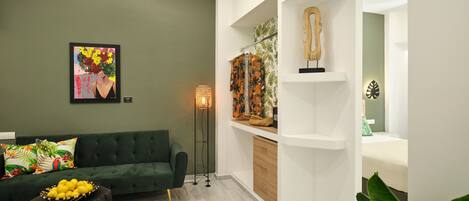 A modern living room with a green sofa, a floor lamp, and a wall-mounted shelf with decorative items.