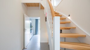 A modern staircase with wooden steps and white railings, leading to an open-plan living area with a kitchen and a view of a blue sky. - Vacation home Fischerhaus in Tönning for up to 6 people (Tönning)