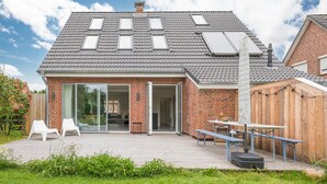 A modern house with a sloped roof, large windows, and a patio area with outdoor seating. - Vacation home Fischerhaus in Tönning for up to 6 people (Tönning)