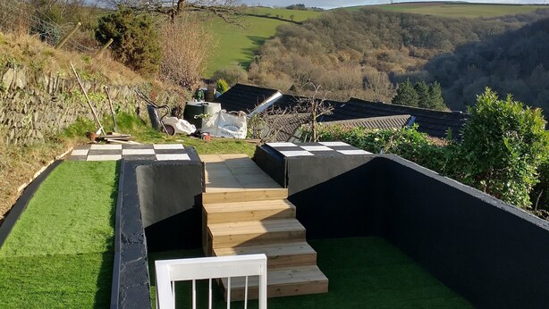 Terraço no telhado com vista para colinas ondulantes, uma árvore e um muro de pedra.
