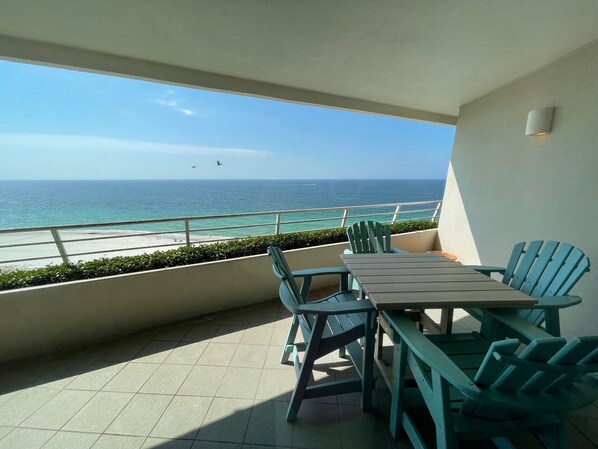 Uma varanda com vista para o mar, uma mesa e cadeiras.