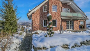 Una casa de ladrillo de dos pisos con tejado cubierto de nieve y un camino de piedra que conduce a la entrada.