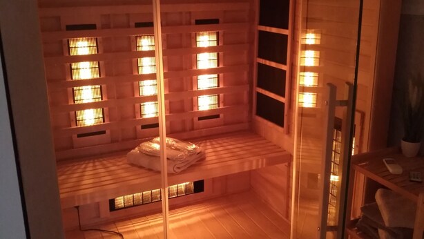 Habitación con piso de madera, una cama y un separador de vidrio. Hay ventanas con persianas y un estante con toallas.
