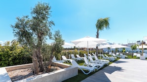 Un espace aménagé au bord de la piscine, avec des chaises longues blanches, des parasols et une pelouse bien entretenue.