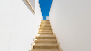 Un escalier droit aux marches de couleur beige, montant vers le haut entre deux murs blancs.