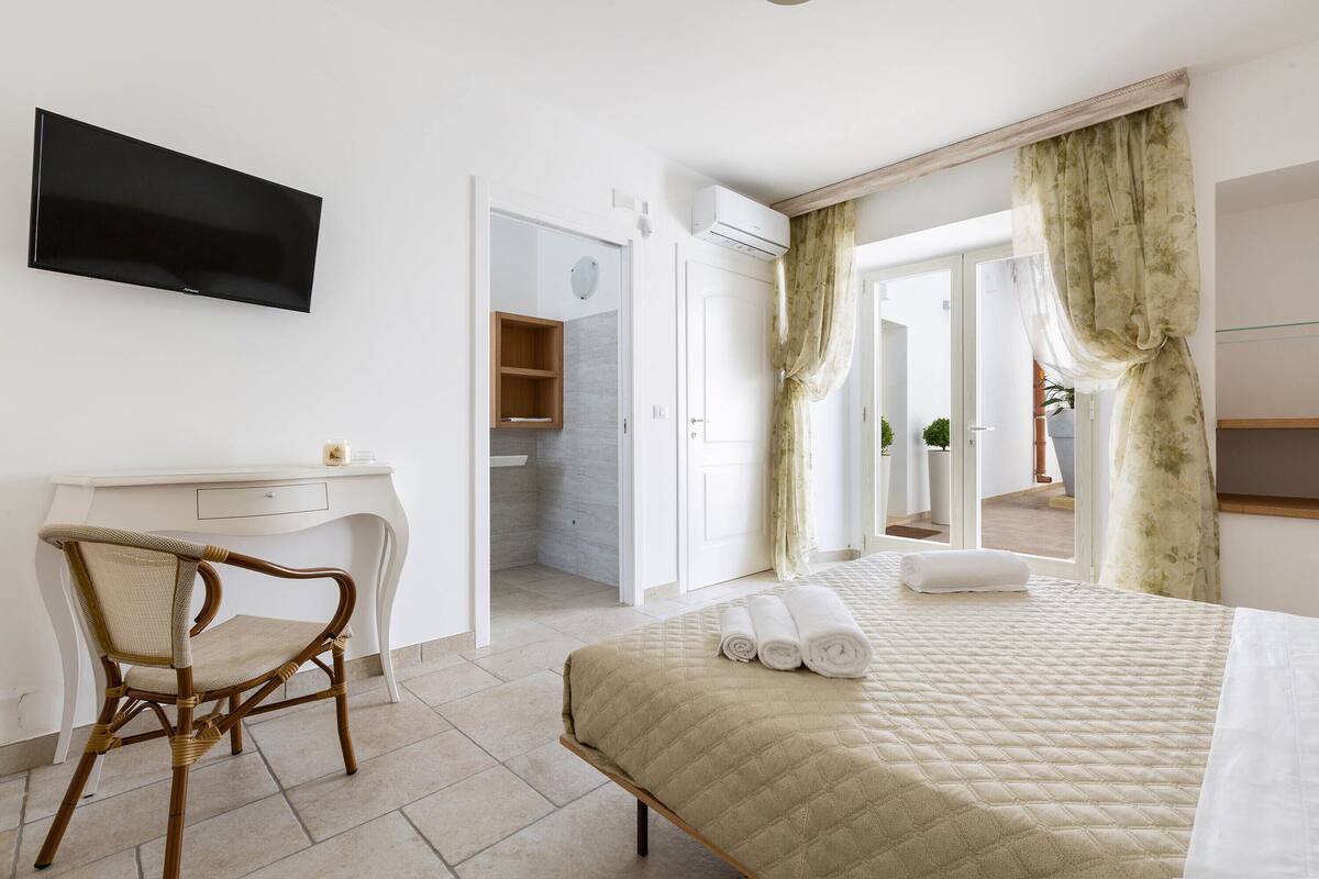 Ein Hotelzimmer mit Bett, Schreibtisch, Stuhl und einem an der Wand befestigten Fernseher.