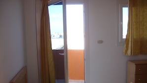 Quarto com cama, mesa de cabeceira, luminária e janela com cortinas.
