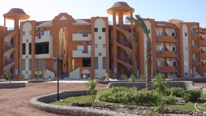 Um hotel com vários andares, com um esquema de cores marcante em laranja e branco, com varandas e um pátio central com paisagismo.