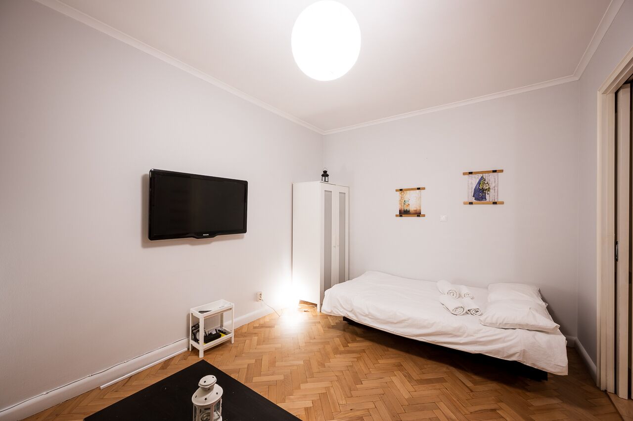 A bedroom with a bed, a television, a wardrobe, and a small shelf with decorative items.