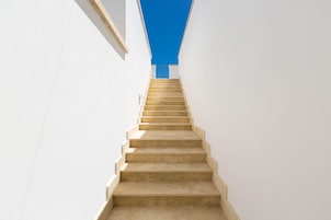 Una escalera recta color beige que sube entre paredes blancas.