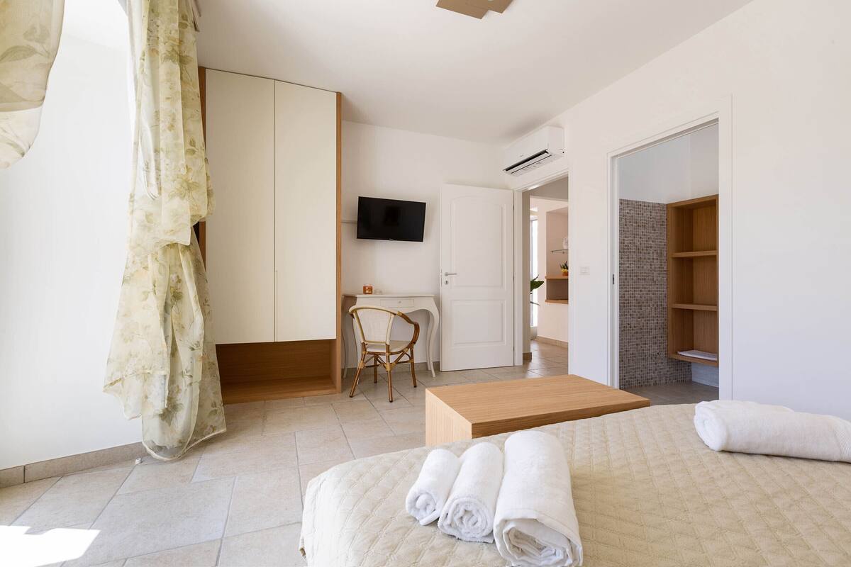 Habitación de hotel con cama, escritorio, silla, televisor y armario.
