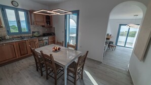Una cocina moderna con armarios de madera, una mesa de comedor y sillas. Se aprecia una vista al exterior a través de amplios ventanales.