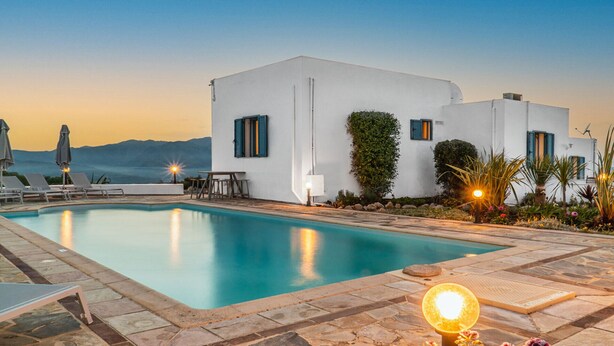 Zona de piscina con vistas despejadas al mar y a las montañas al atardecer.