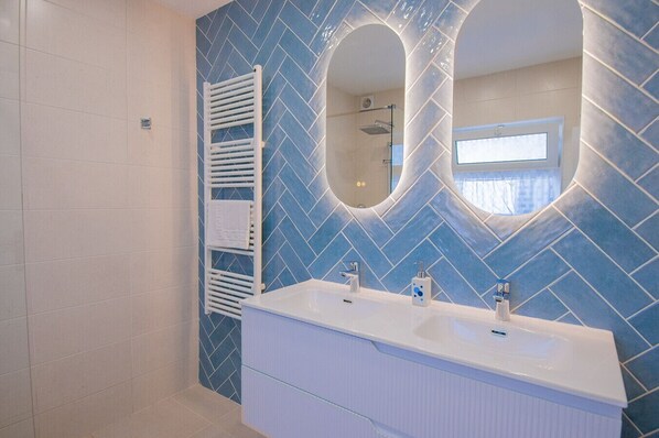 Een badkamer met twee wastafels, een witte handdoekhouder en een blauwe backsplash van herringbone tegels.