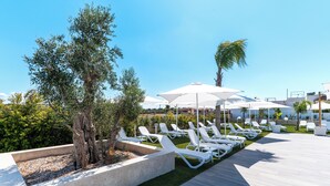 Ein Poolbereich mit weißen Liegestühlen, Sonnenschirmen und einem gepflegten Rasen.