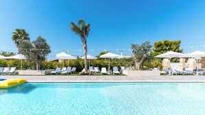 Ein Poolbereich mit Liegestühlen und Sonnenschirmen, umgeben von Bäumen und blauem Himmel.