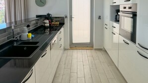 A modern kitchen with a black countertop, stainless steel appliances, and a wooden floor. - Self contained forest view luxury apartments  (Kusadasi)