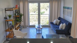 A modern living room with a blue sofa, a white chair, a small wooden table, and a kitchen area with a black countertop. - Self contained forest view luxury apartments  (Kusadasi)