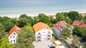 Ein Wohngebiet mit Blick auf den Strand, mit Häusern mit roten Dächern und Balkonen, umgeben von viel Grün.