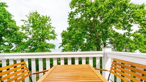 Eine Holzterrasse mit weißen Geländern und zwei hölzernen Bänken, die auf eine üppige, grüne Landschaft blicken.